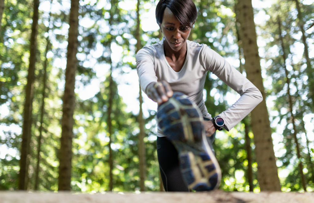 Young female runner warming up before running in forest.